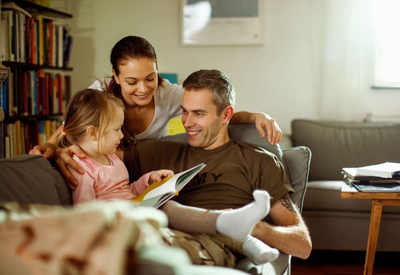 U.S. Army veteran at home reading with his wife and young daughter